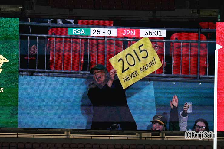 「2015 NEVER AGAIN!」のプラカードを持って応援するサポーター